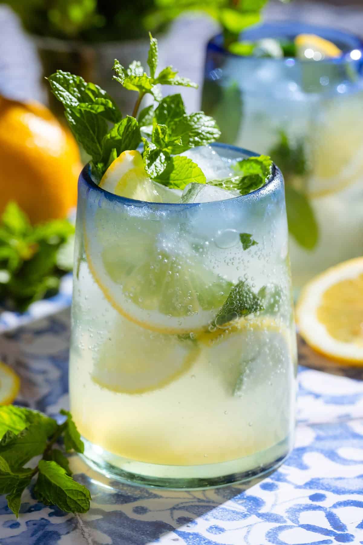 A lemon mocktail in a short glass with a blue rim garnished with lemon slices and fresh mint.