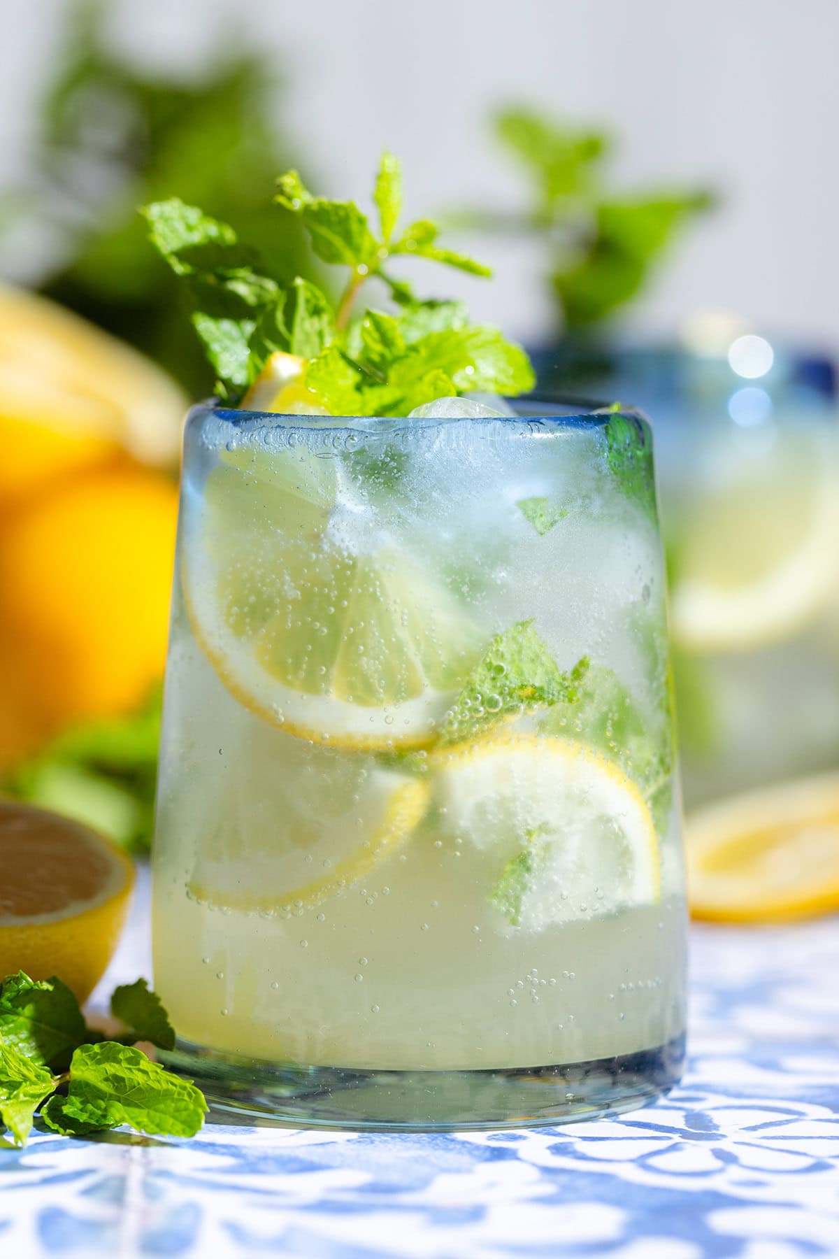 A lemon mocktail in a short glass with a blue rim garnished with lemon slices and fresh mint.