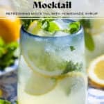 A lemon mocktail in a short glass with a blue rim garnished with lemon slices and fresh mint.