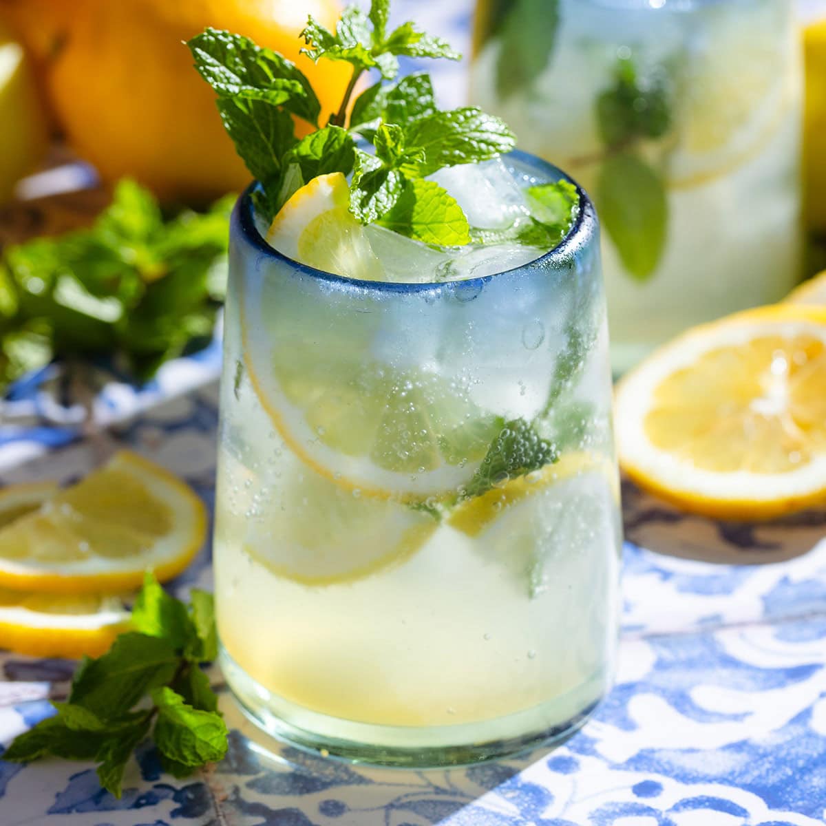 A lemon mocktail in a short glass with a blue rim garnished with lemon slices and fresh mint.