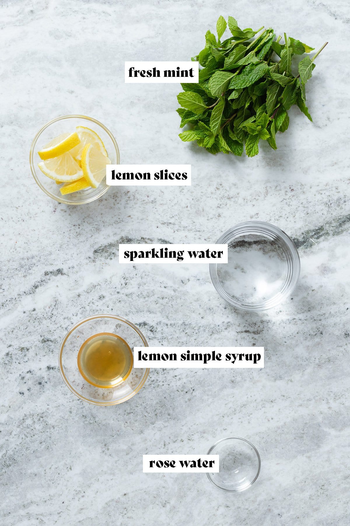 Fresh mint, lemon slices, lemon simple syrup, sparkling water, and rose water in small glass bowls.