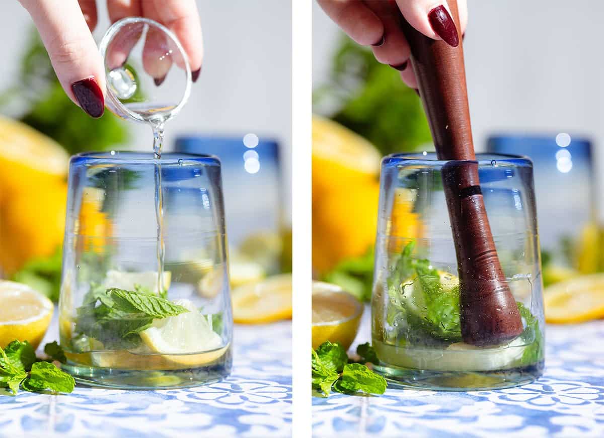 A hand adding rose water into a short glass with fresh mint and lemon slices and muddling everything using a wooden muddler.