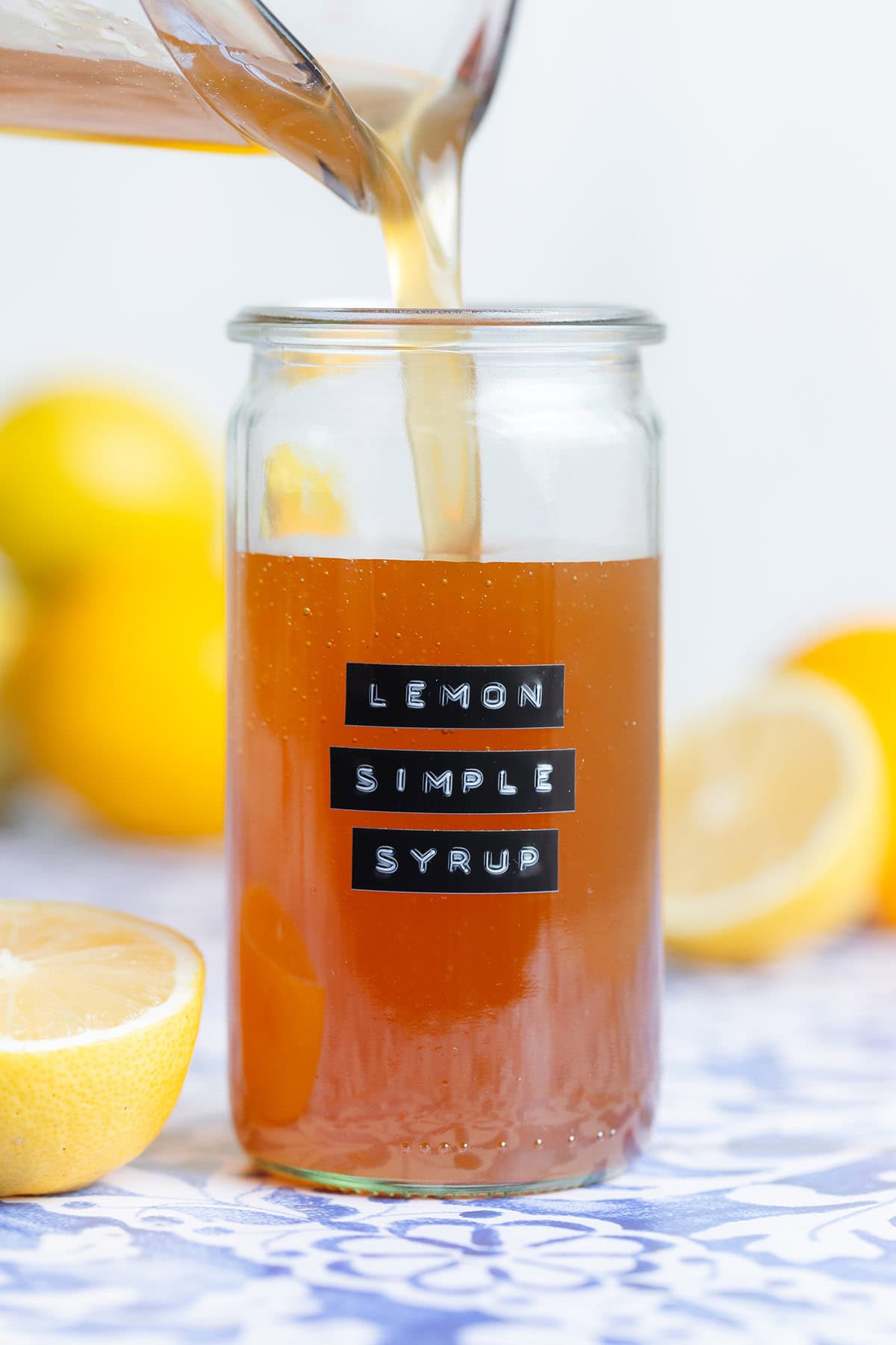 Orange colored lemon syrup being poured into a tall glass jar.