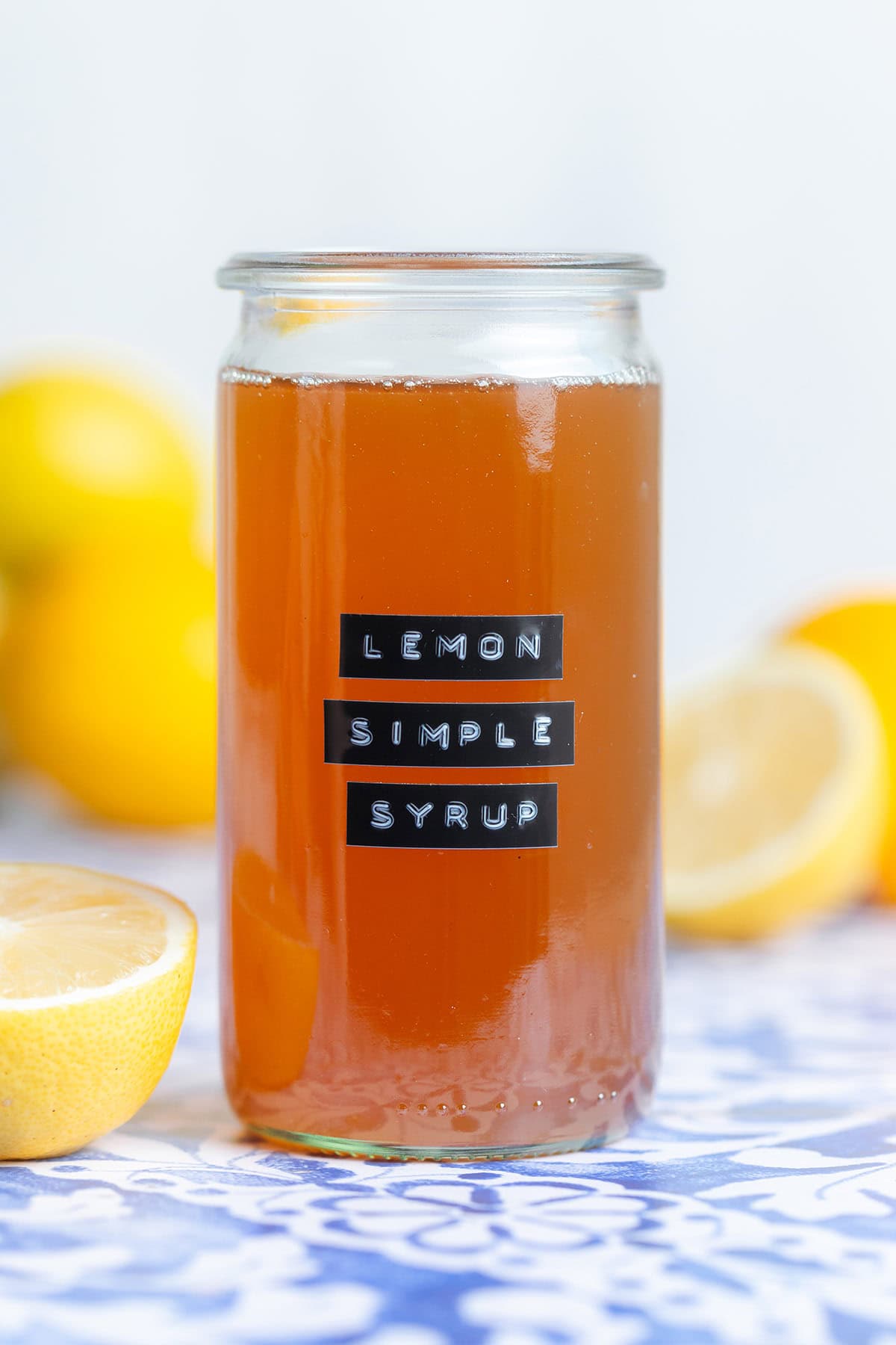 Orange colored lemon syrup in a tall glass jar without a lid with a black embossed label.