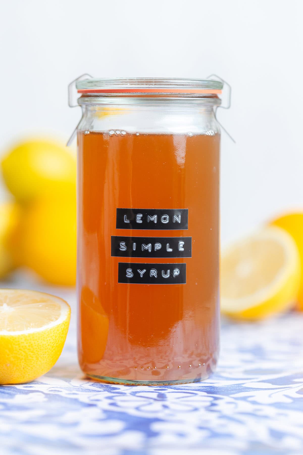 Orange colored syrup in a tall glass jar with a black embossed label that says lemon simple syrup.