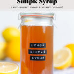 Orange colored lemon syrup in a tall glass jar with a black embossed label.