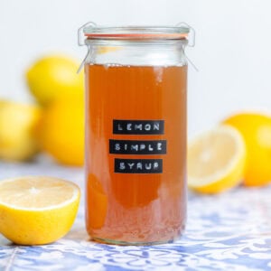 Orange colored lemon syrup in a tall glass jar with a black embossed label.