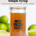Dark yellow syrup in a glass jar with a black embossed label that says lime simple syrup with limes all around.