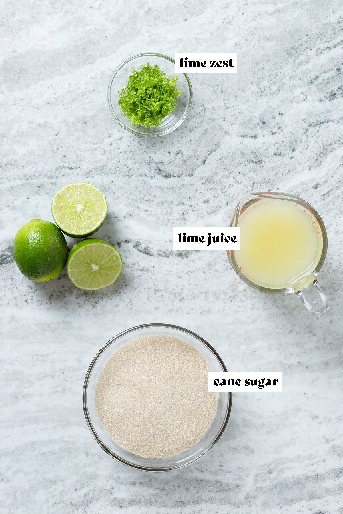 Cane sugar, lime juice, and lime zest measured in bowls and a measuring cup with whole limes on the left.