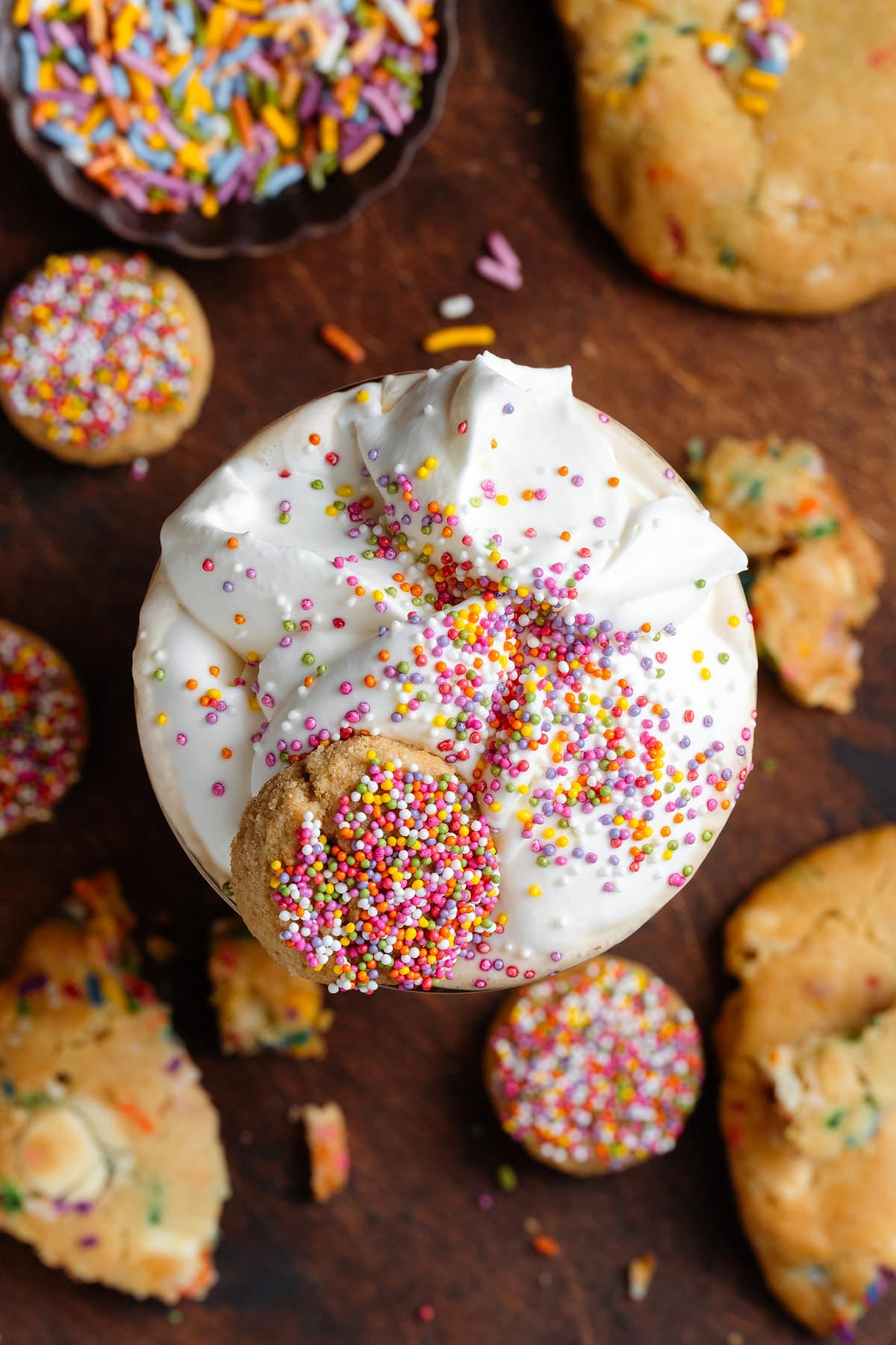 Iced latte in a tall glass with homemade whipped cream, sprinkles, and a small cookie on top.