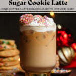 Iced latte in a tall glass with a thick gold stem topped with whipped cream, sprinkles, and a small cookie.