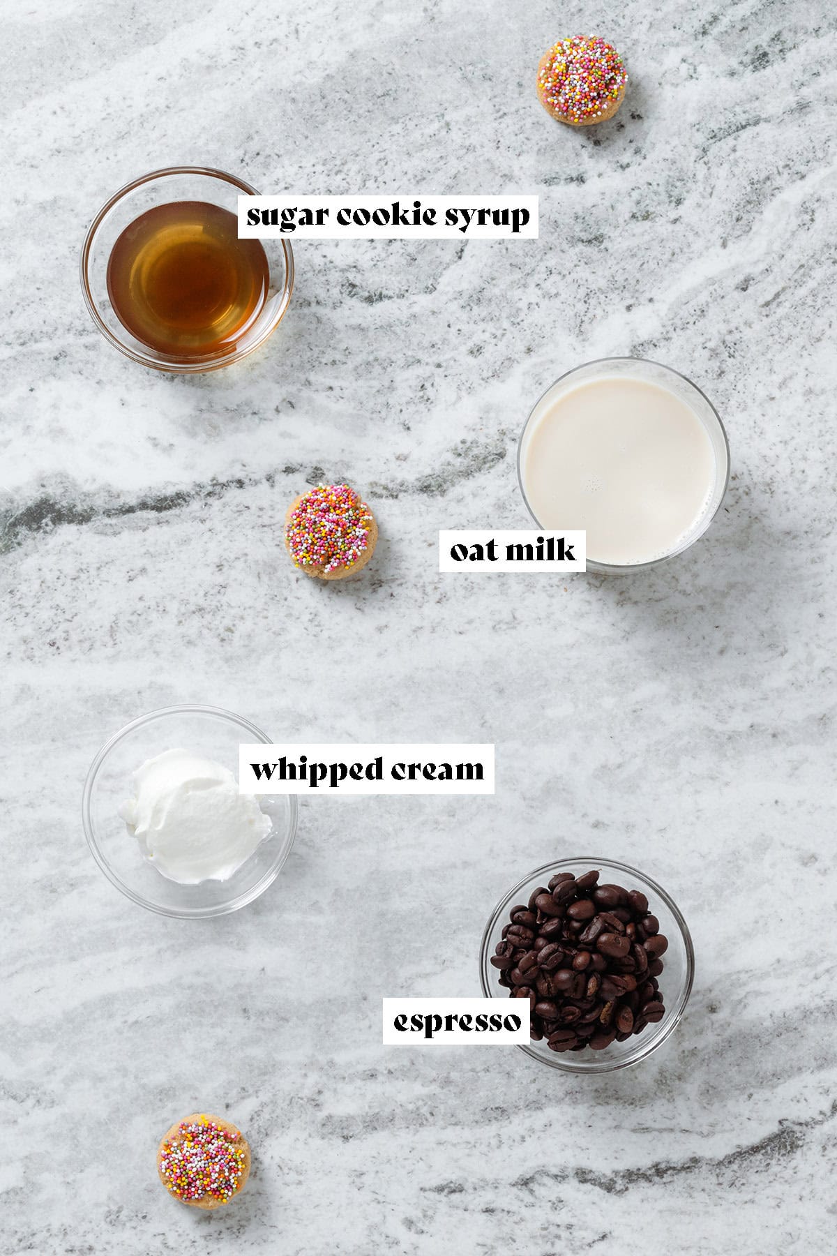 Sugar cookie syrup, oat milk, whipped cream, and coffee beans in small glass bowls.