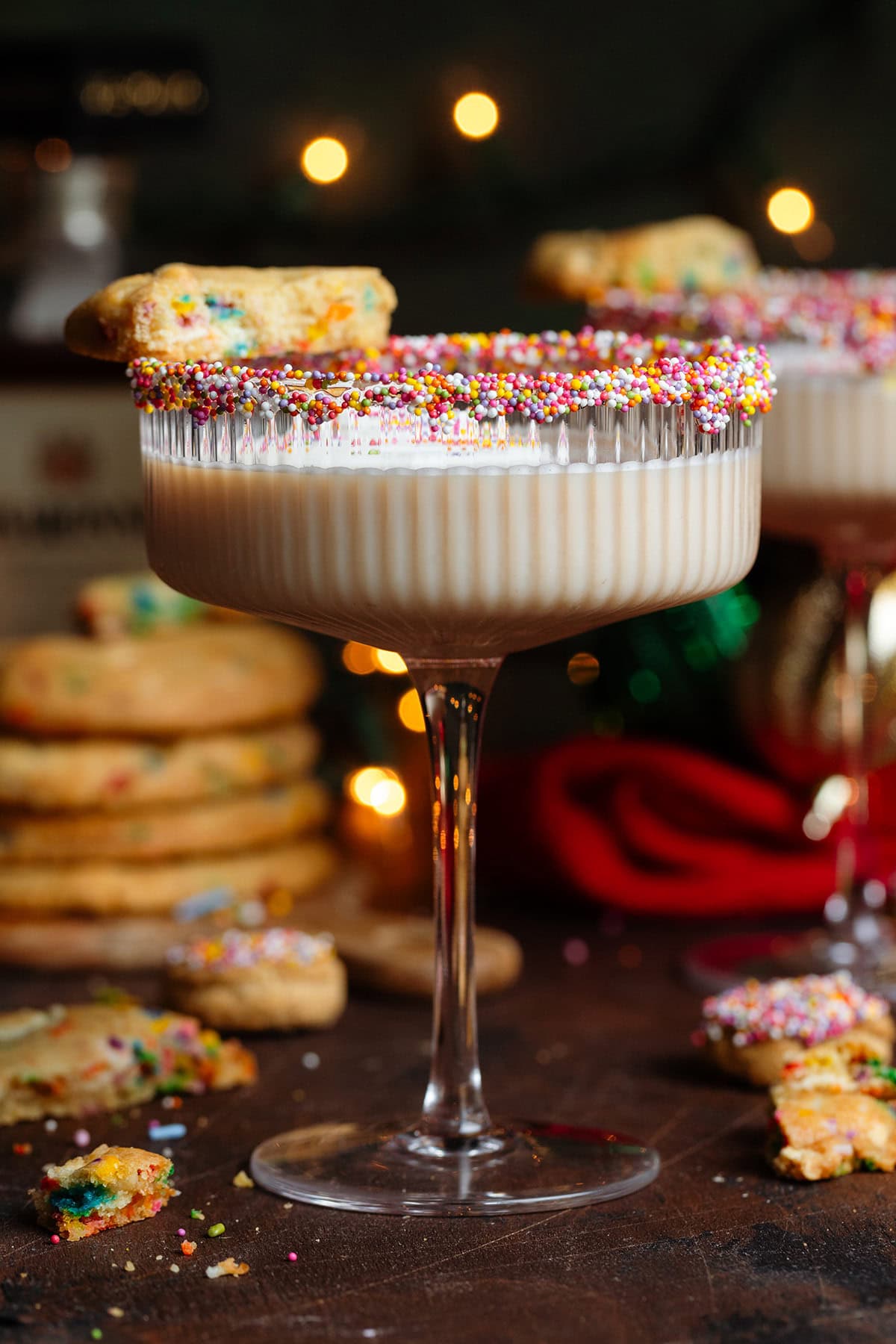 A creamy beige cocktail in a coupe glass with sprinkles on the rim and half of a cookie resting on the rim.