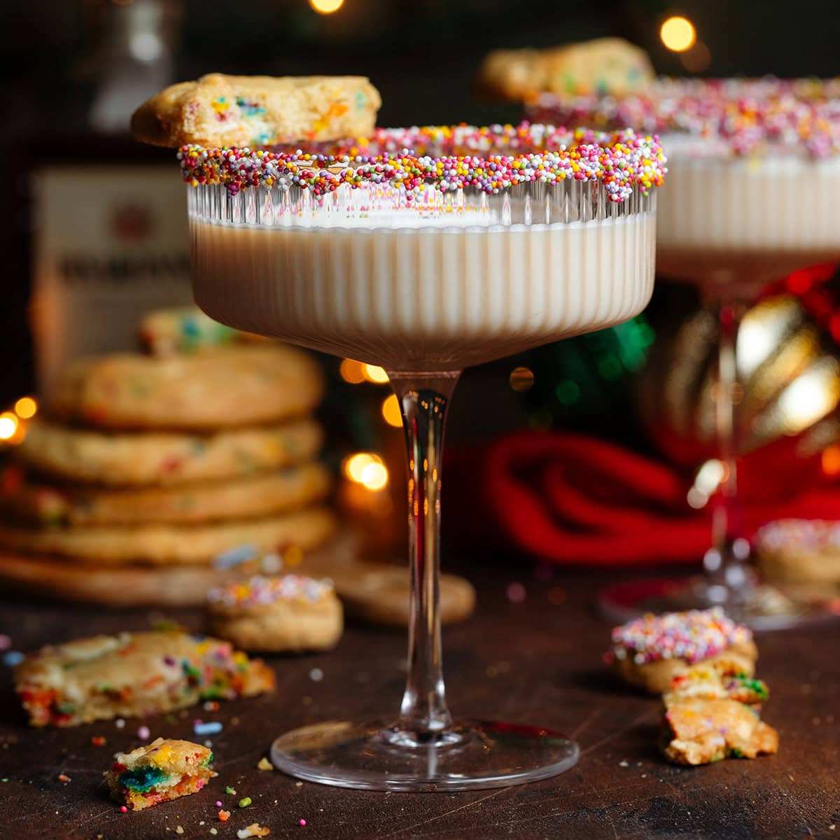 A creamy beige cocktail in a coupe glass with sprinkles on the rim and half of a cookie resting on the rim.