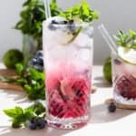 A tall glass with blueberry mojito with an ombre effect with the purple settling on the bottom.
