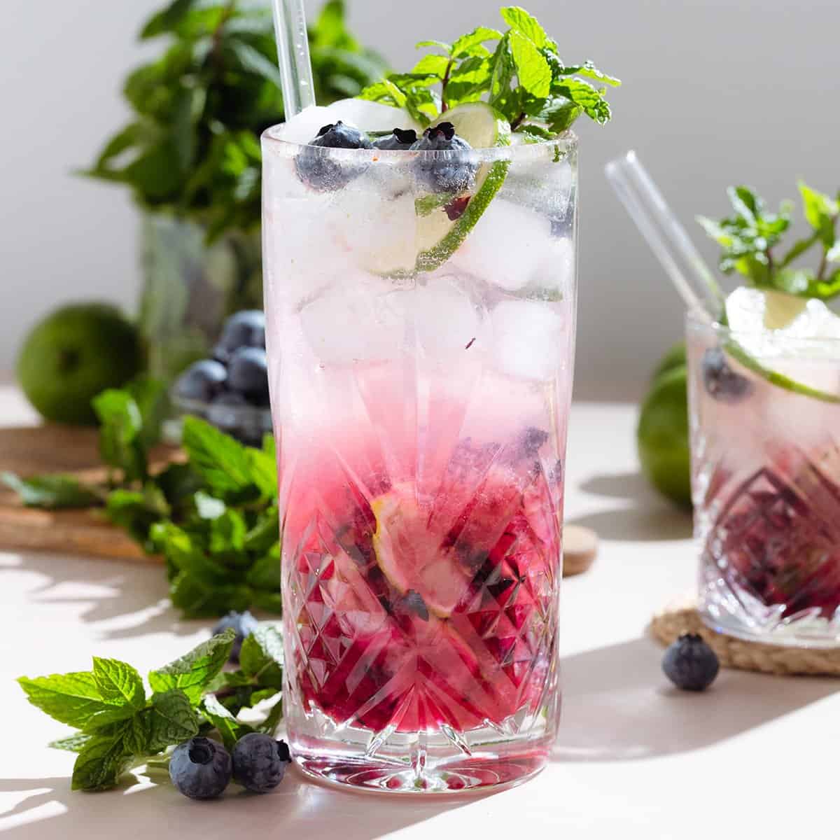 A tall glass with blueberry mojito with an ombre effect with the purple settling on the bottom.