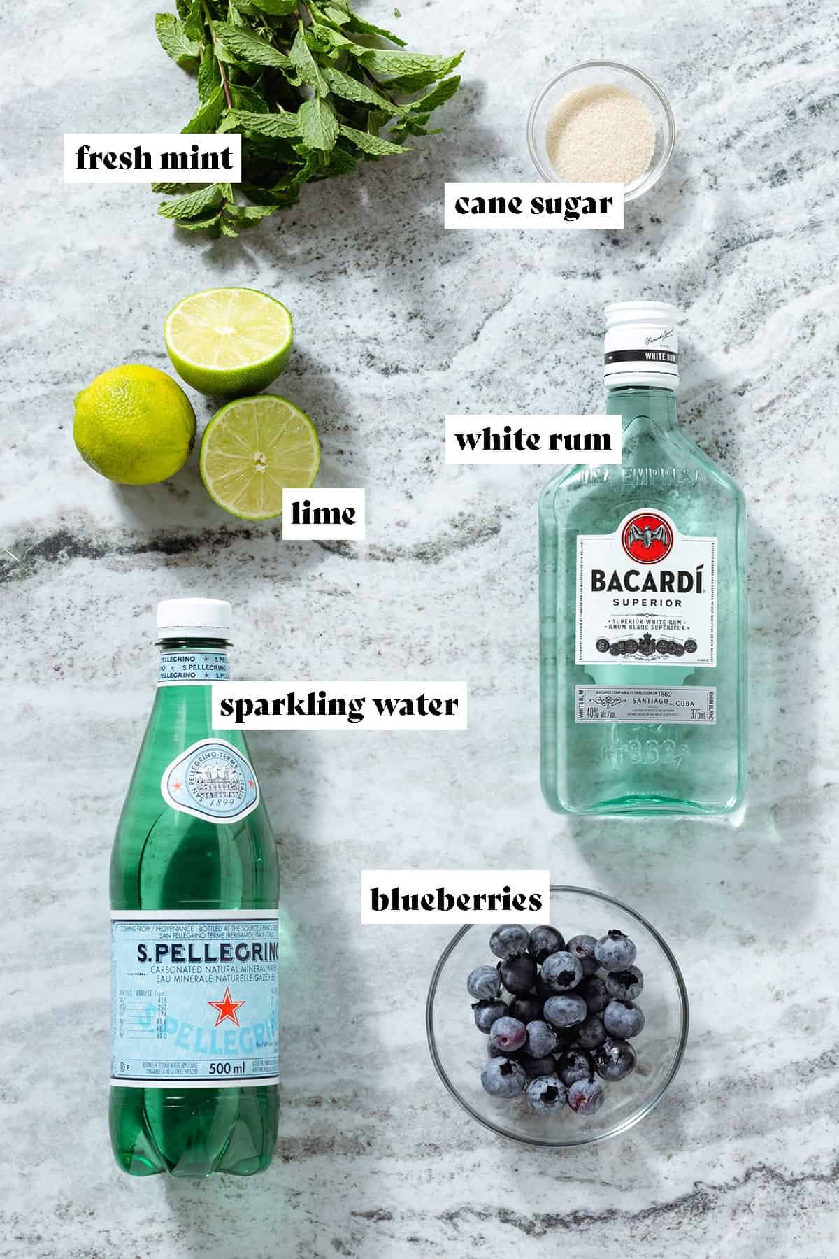 Ingredients like limes, fresh mint, sparking water, and white rum laid out.