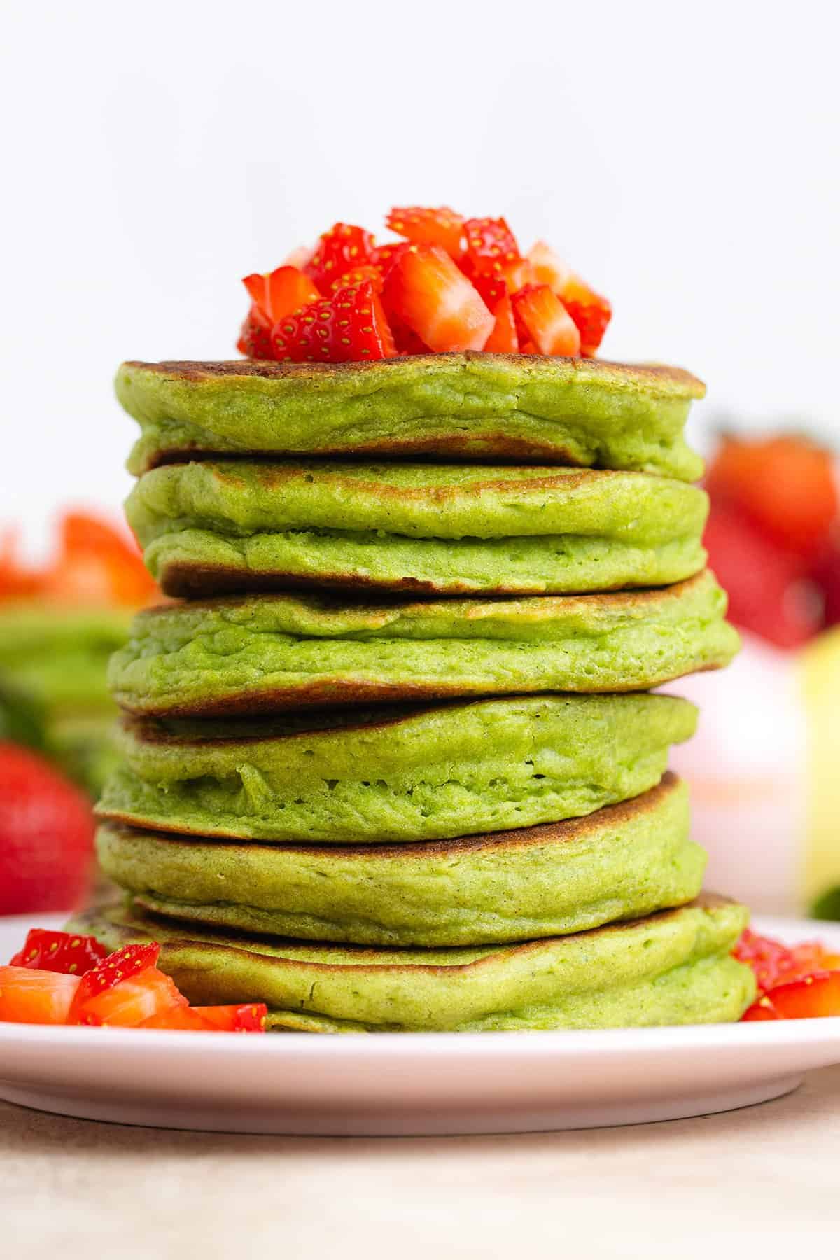 A stack of green pancakes topped with chopped strawberries.