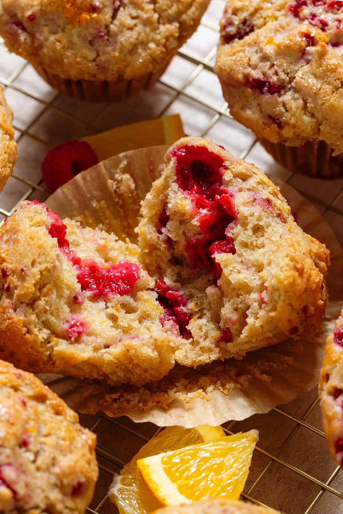 A muffin with raspberries and orange zest torn in half to show the fluffy inside on a muffin paper cup.
