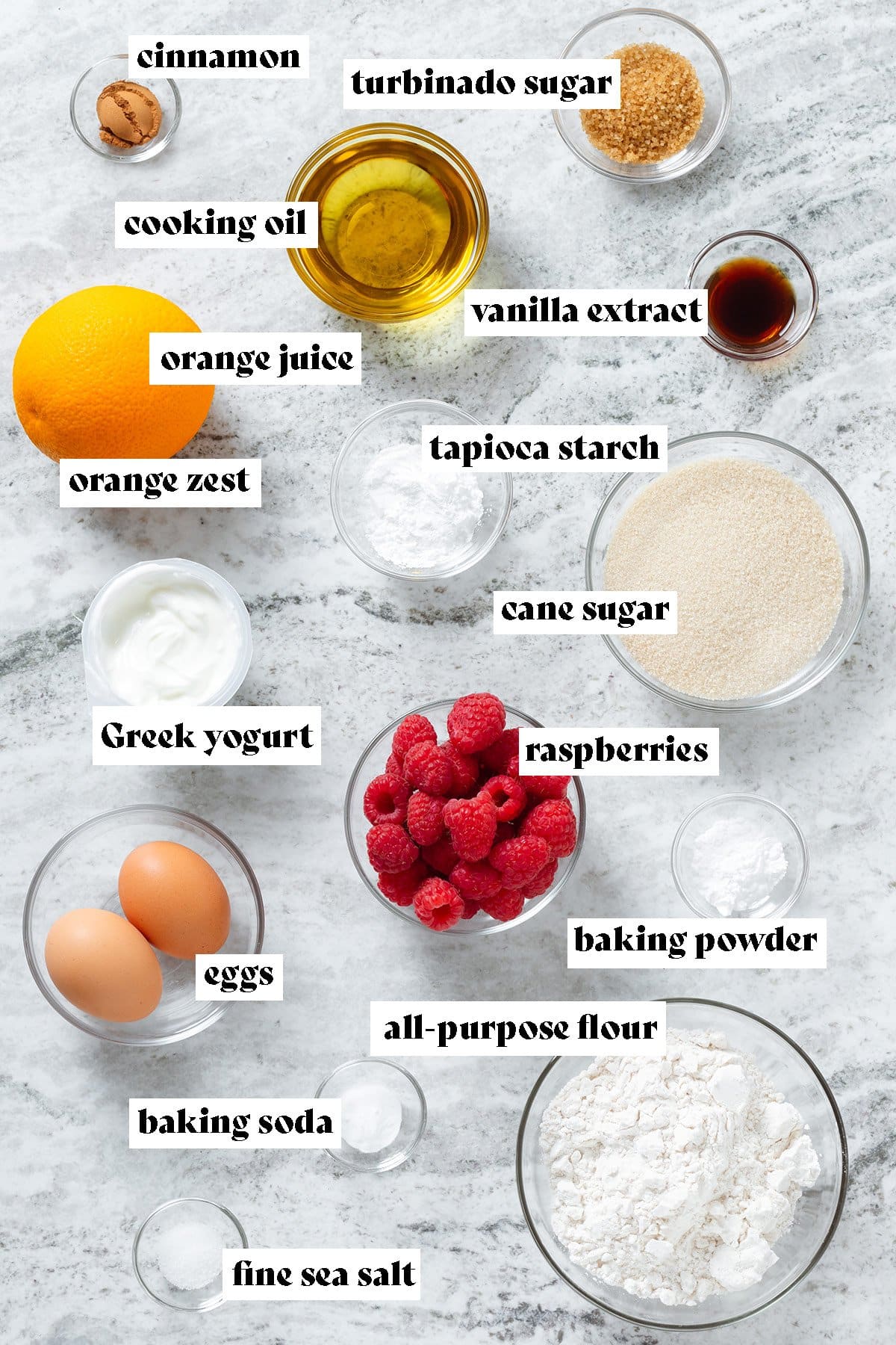Ingredients like eggs, flour, sugar, oil, raspberries, and an orange all laid out.