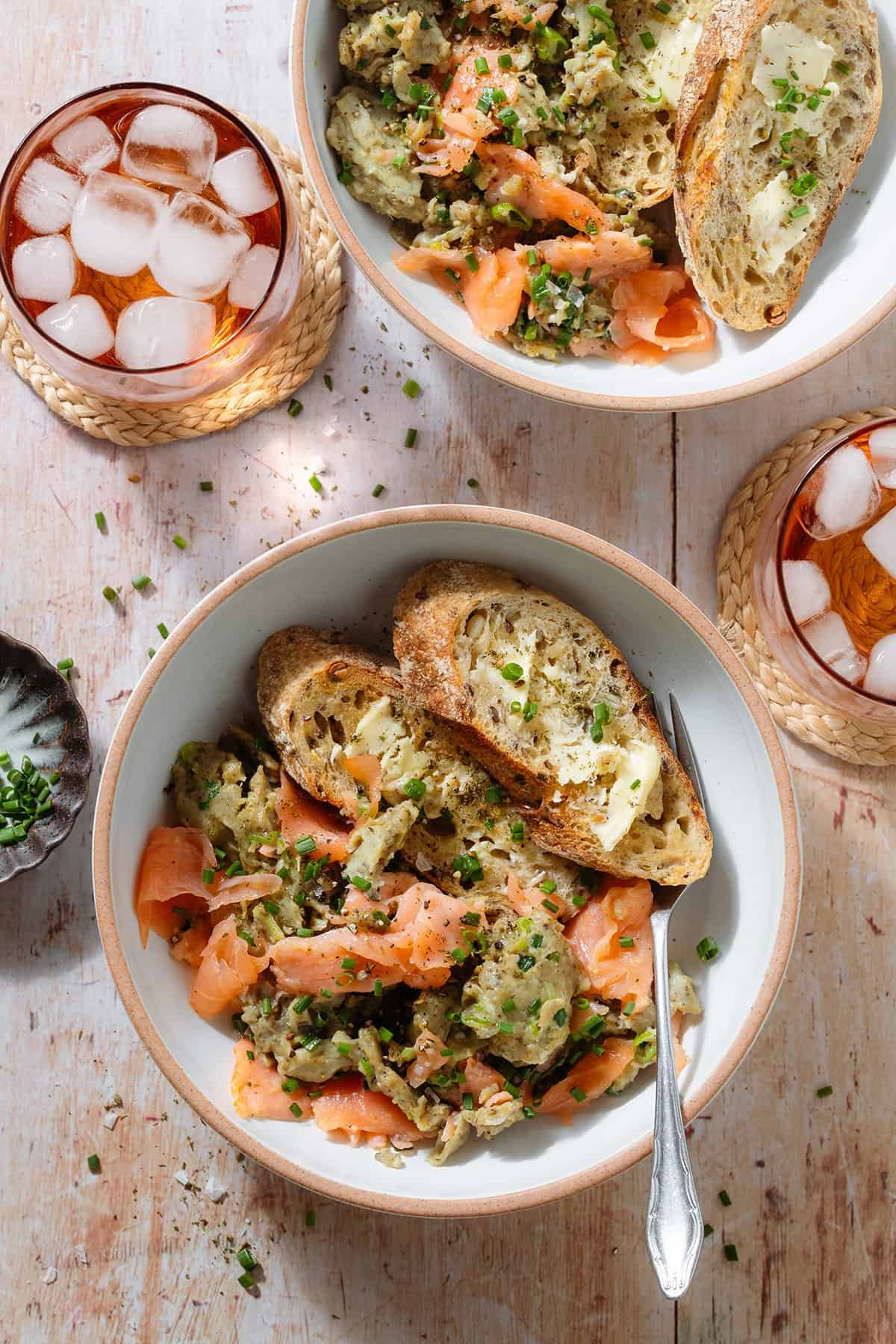 Scrambled eggs with smoked salmon in a white low bowls with large toasted and buttered slices of baguette.