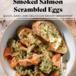 Scrambled eggs with smoked salmon in a white low bowl with toasted and buttered thick baguette slices and a fork.