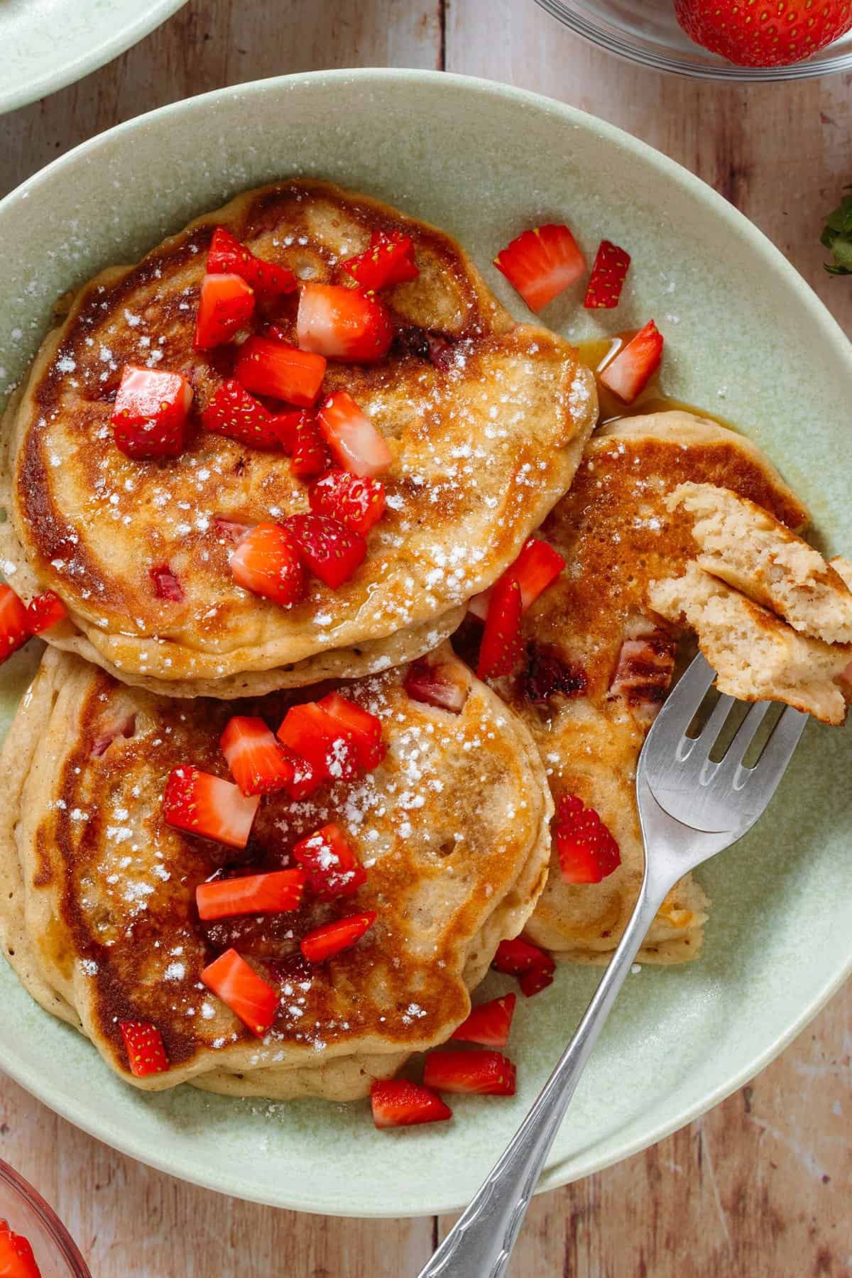 Pancakes with fresh strawberries with a fork holding a bite of the pancakes to show the inside.