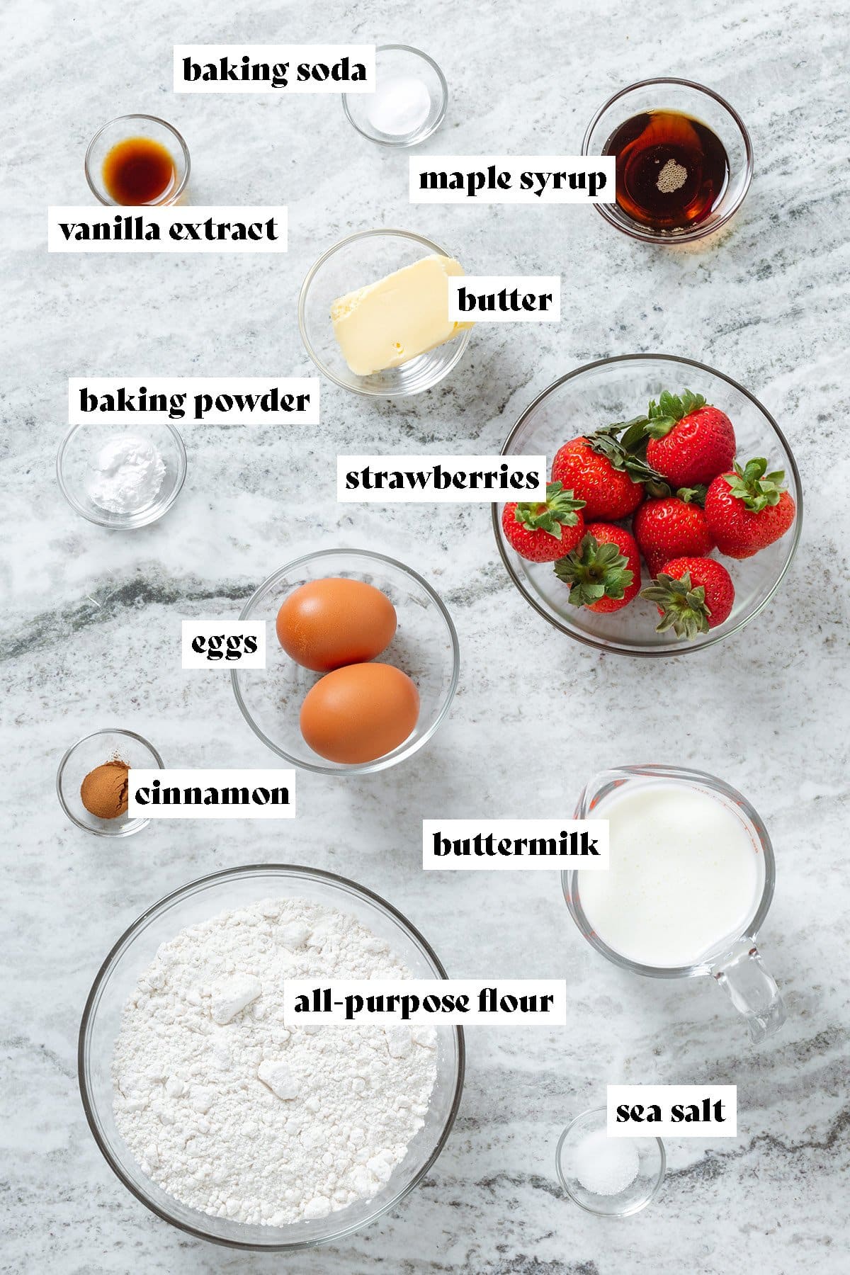 Measured ingredients in glass bowls like flour, strawberries, eggs, buttermilk, maple syrup, and baking powder.