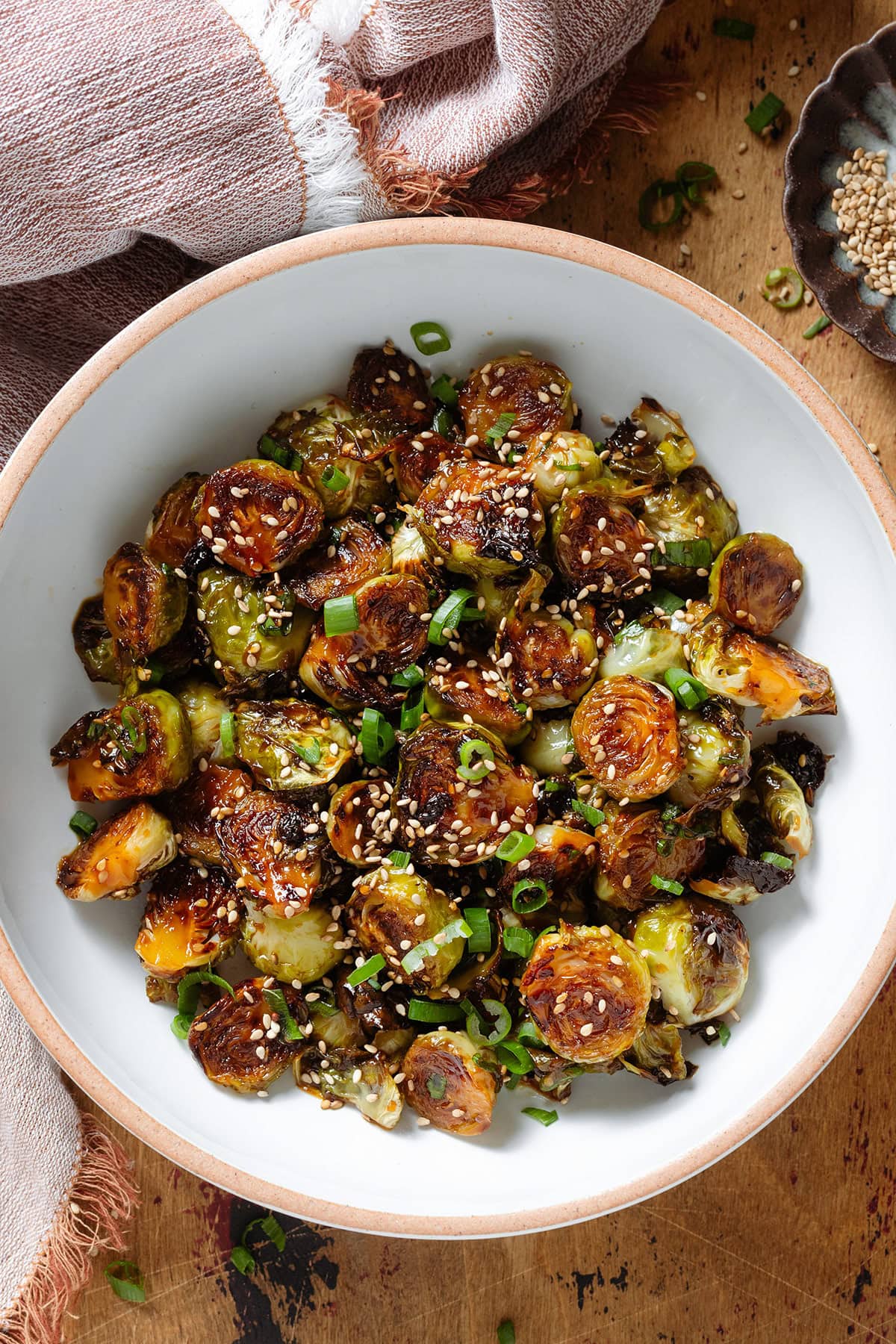 Roasted brussels sprouts sprinkled with sesame seeds and green onion in a white bowl with a beige rim.