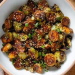 Roasted brussels sprouts with caramelized teriyaki sauce sprinkled with sesame seeds and green onion in a white bowl.