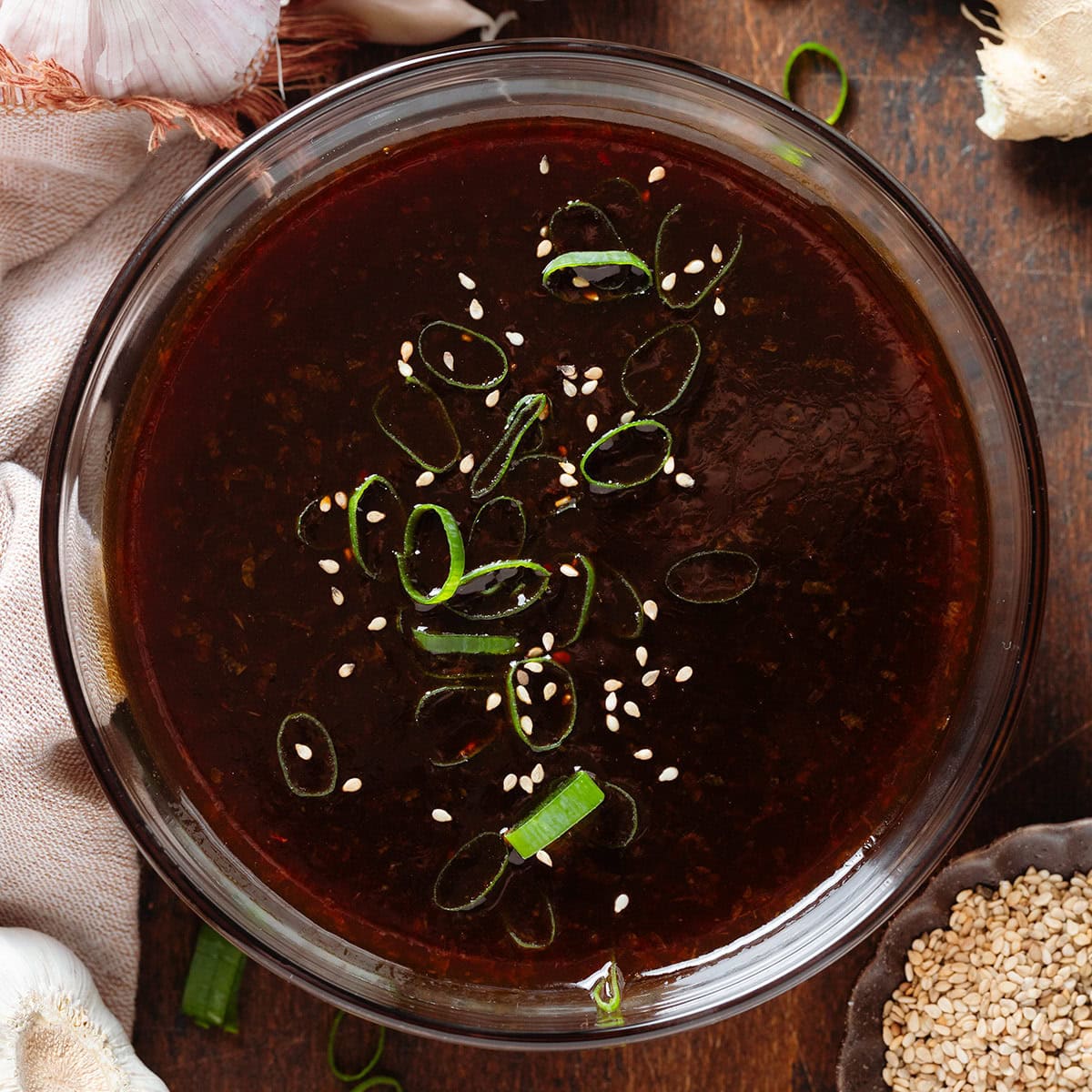 Dark teriyaki sauce in a glass bowl garnished with green onion and sesame seeds.