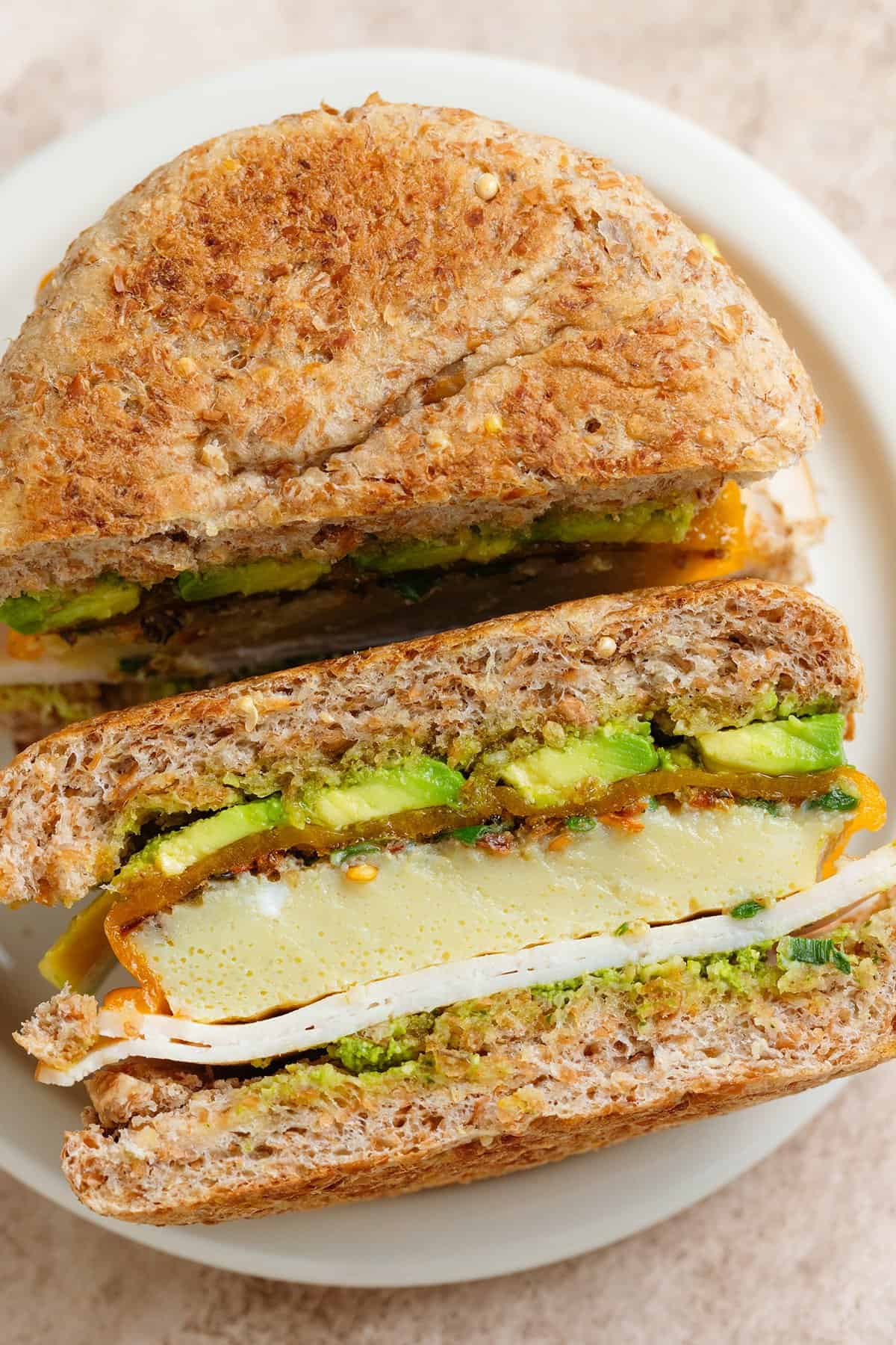 A turkey and egg sandwich with avocado and cheese sliced in half showing the inside.