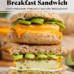 Two breakfast sandwiches with eggs, ham, melted cheese, and avocado stacked on top of each other, the bottom one cut in half showing the inside.