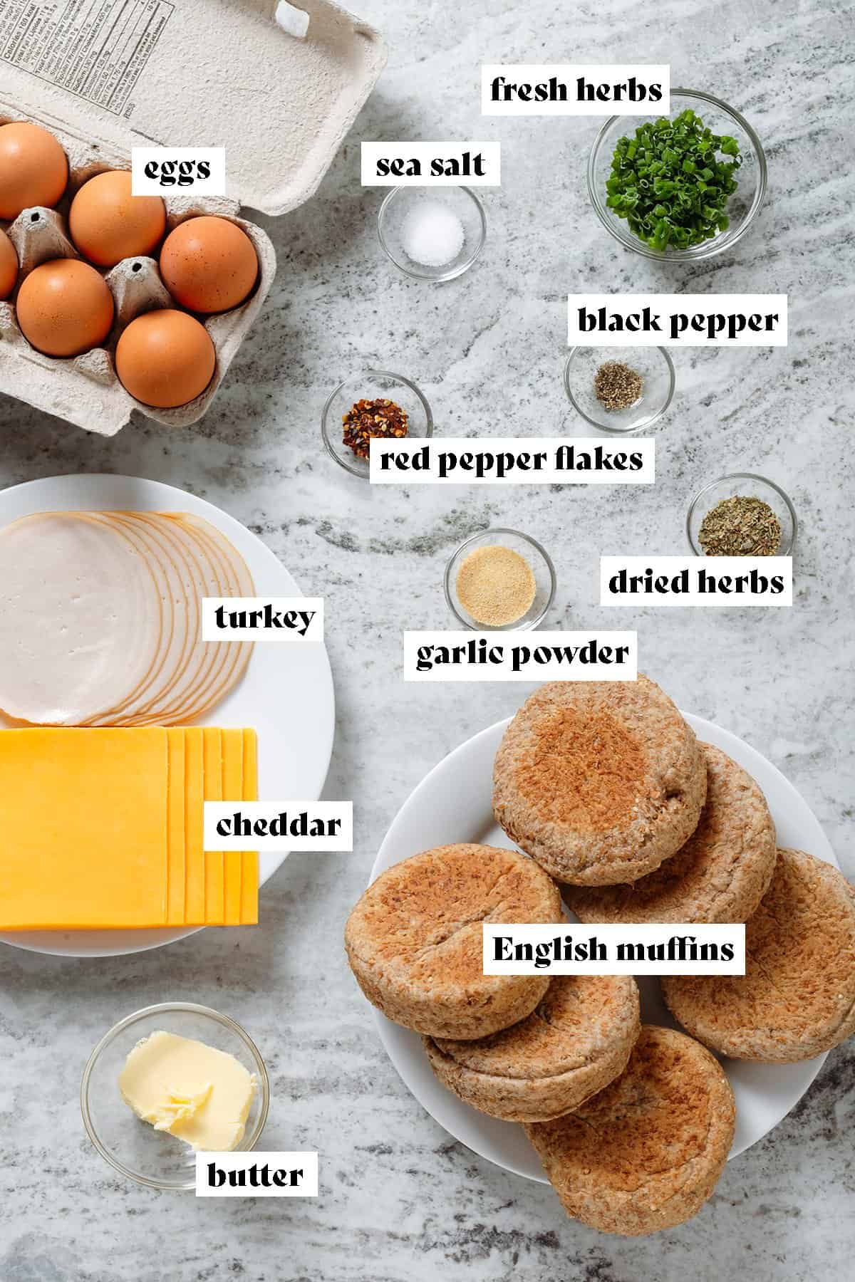 Ingredients like English muffins, sliced cheddar and turkey, eggs, spices, and butter all laid out.