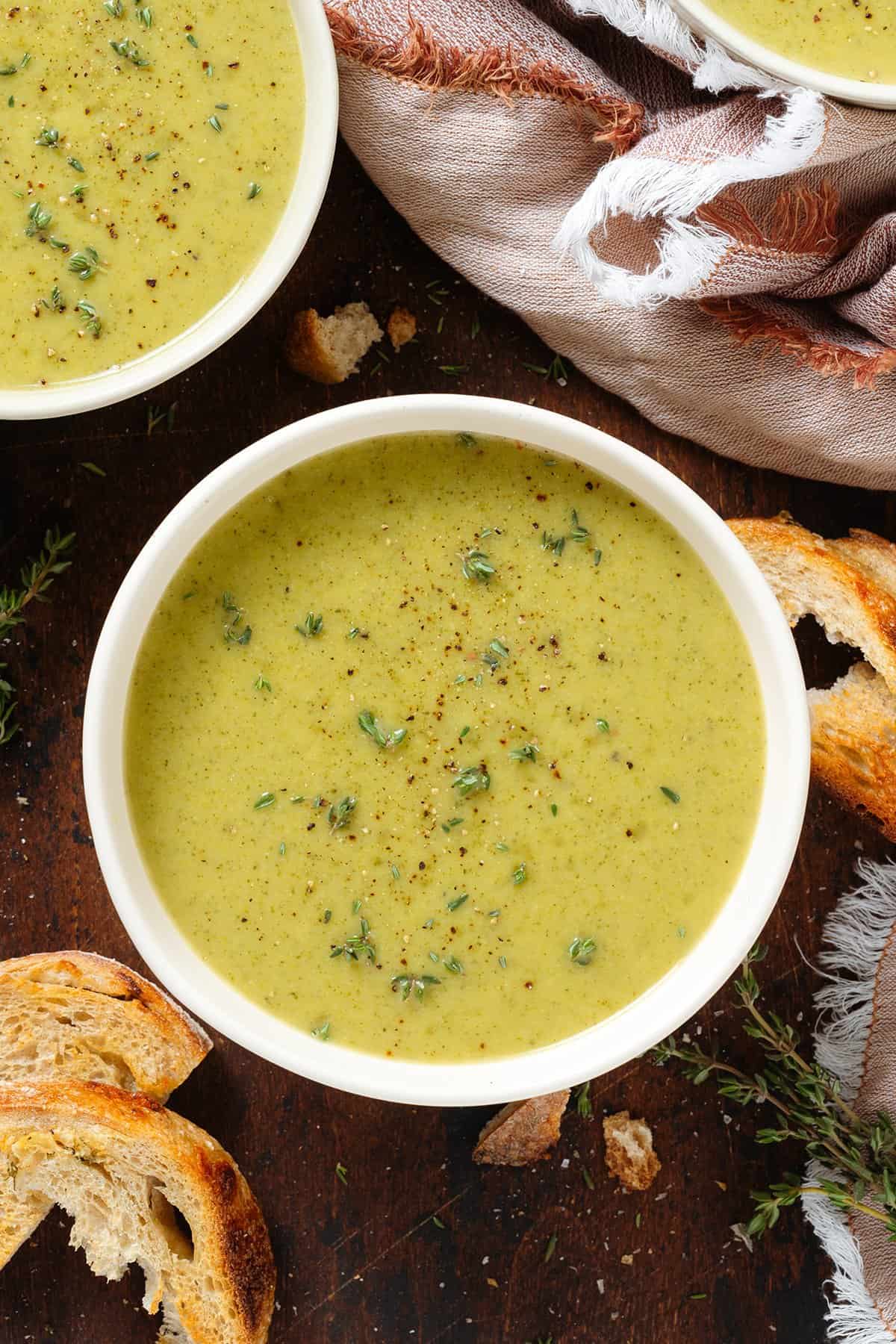 Creamy green broccoli soup in white bowls garnished with fresh thyme and black pepper.