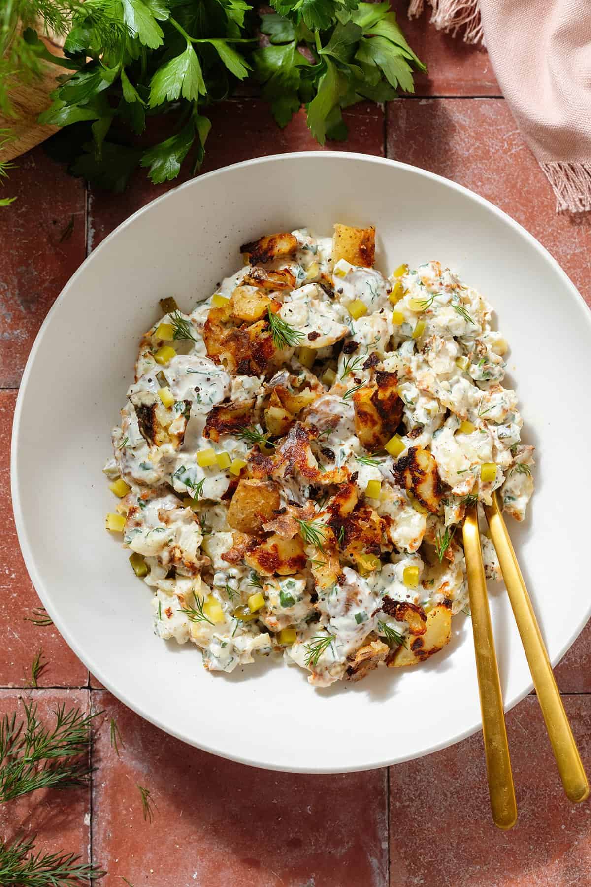 Crispy potato salad with yogurt mayo dressing garnished with bit of more crispy potatoes and fresh dill in a white bowl.