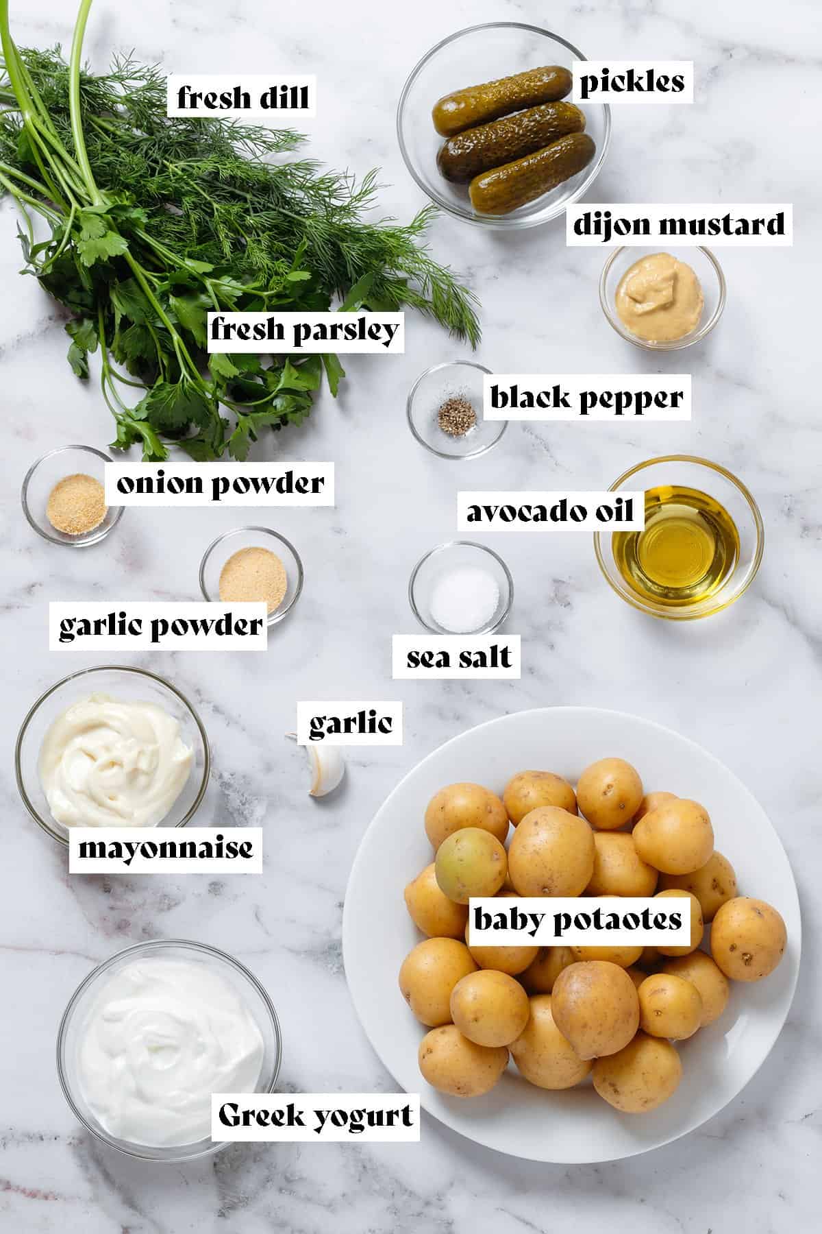 Ingredients like baby potatoes, fresh herbs, pickles, mayonnaise, yogurt, and spices in small bowls on a marble background.
