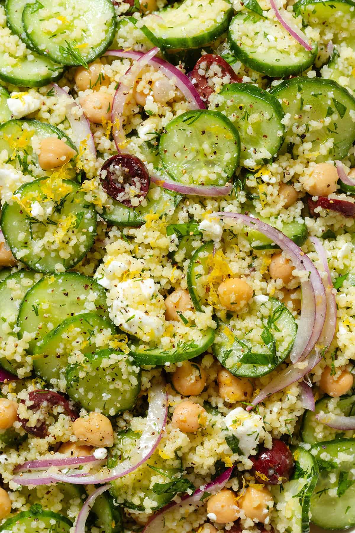 A close up of cucumber and couscous salad with red onion and lemon zest.