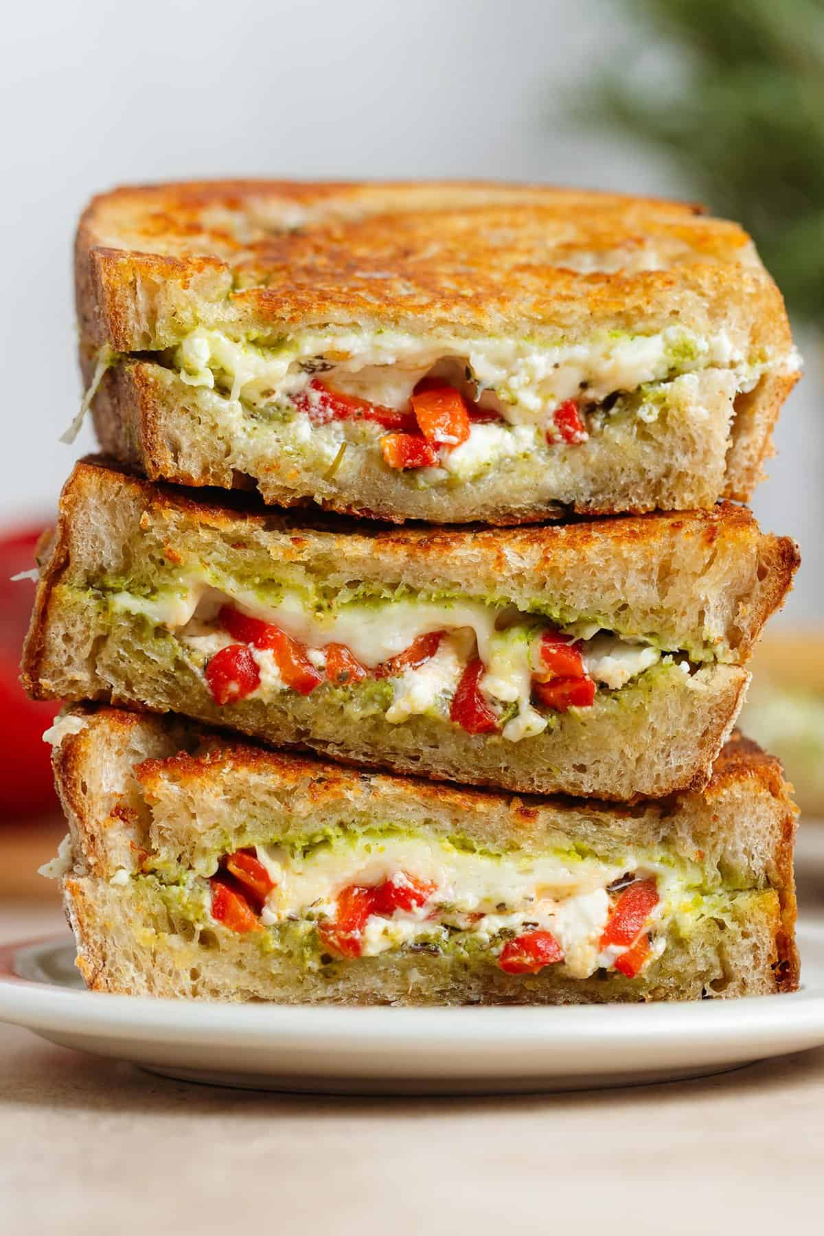 Three slices of grilled cheese with red peppers and pesto stacked on top of each other showing what's inside.