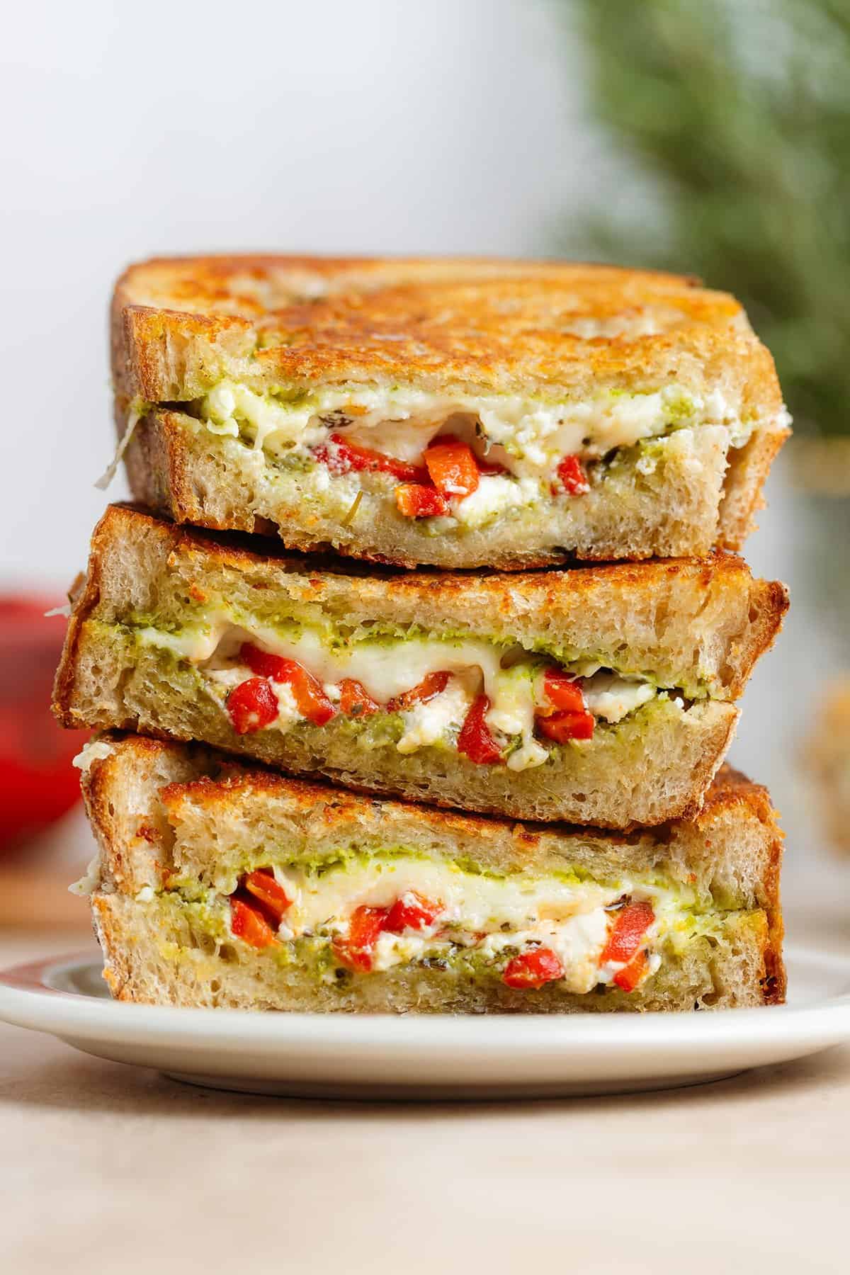 Three slices of grilled cheese with red peppers and pesto stacked on top of each other showing what's inside.