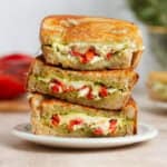 Three slices of grilled cheese with red peppers and pesto stacked on top of each other showing what's inside.