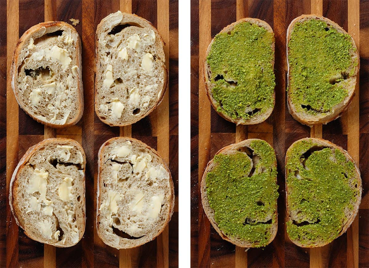 Slices of bread with butter on one side and pesto on the other side on a wooden cutting board.
