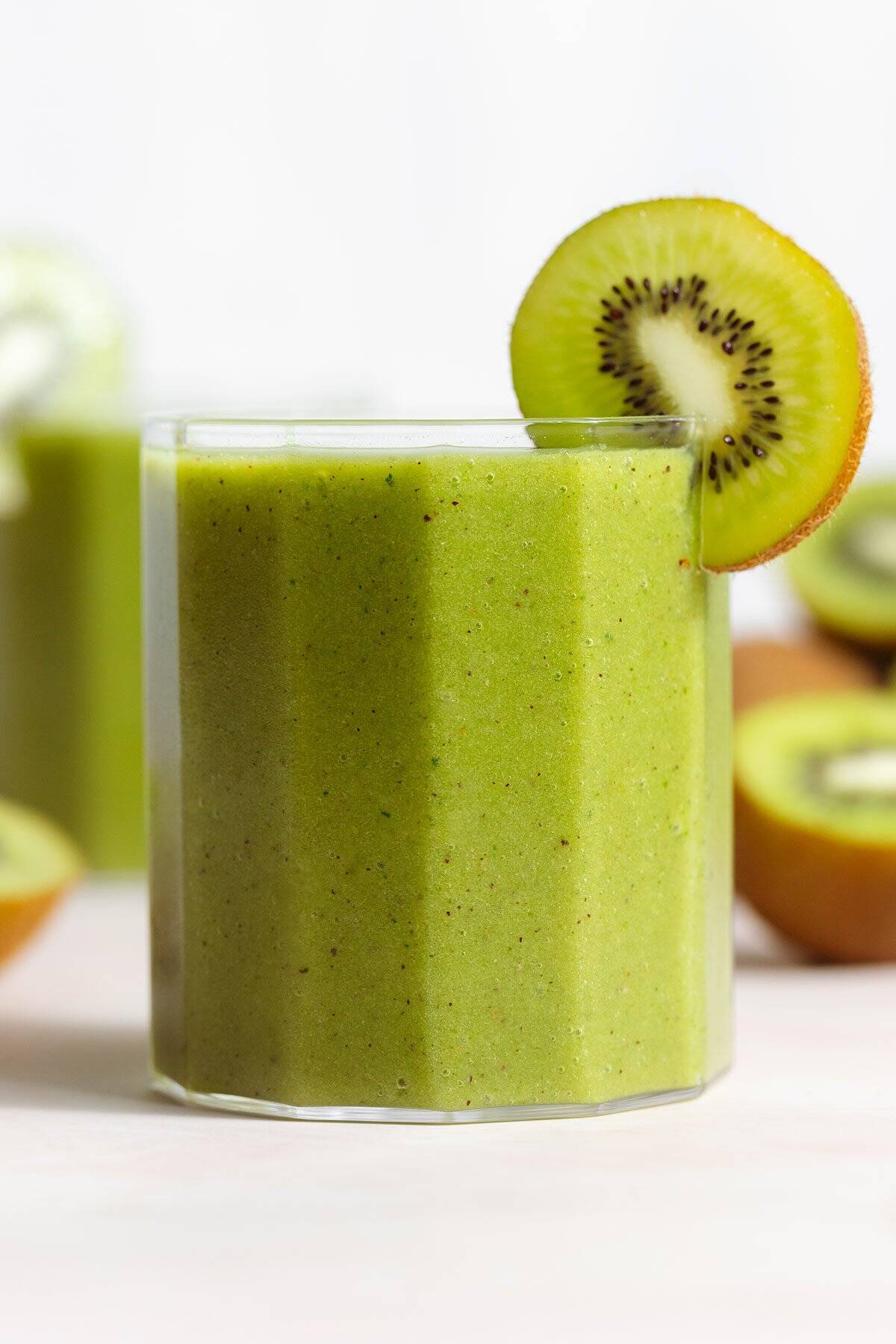 Bright green smoothie in a short glass garnished with a slice of kiwi.
