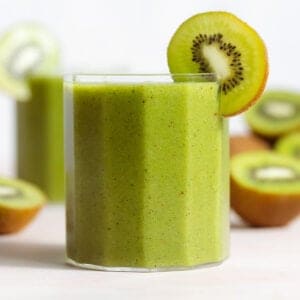 Bright green smoothie in a short glass garnished with a slice of kiwi.