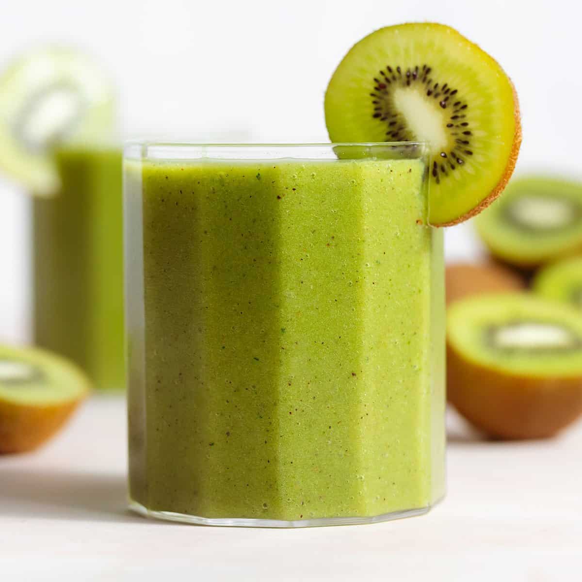 Bright green smoothie in a short glass garnished with a slice of kiwi.