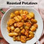 Crispy roasted potatoes in a white low bowl on a tile background with a silver spoon in the bowl.
