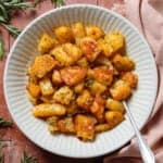 Crispy roasted potatoes in a white low bowl on a tile background with a silver spoon in the bowl.