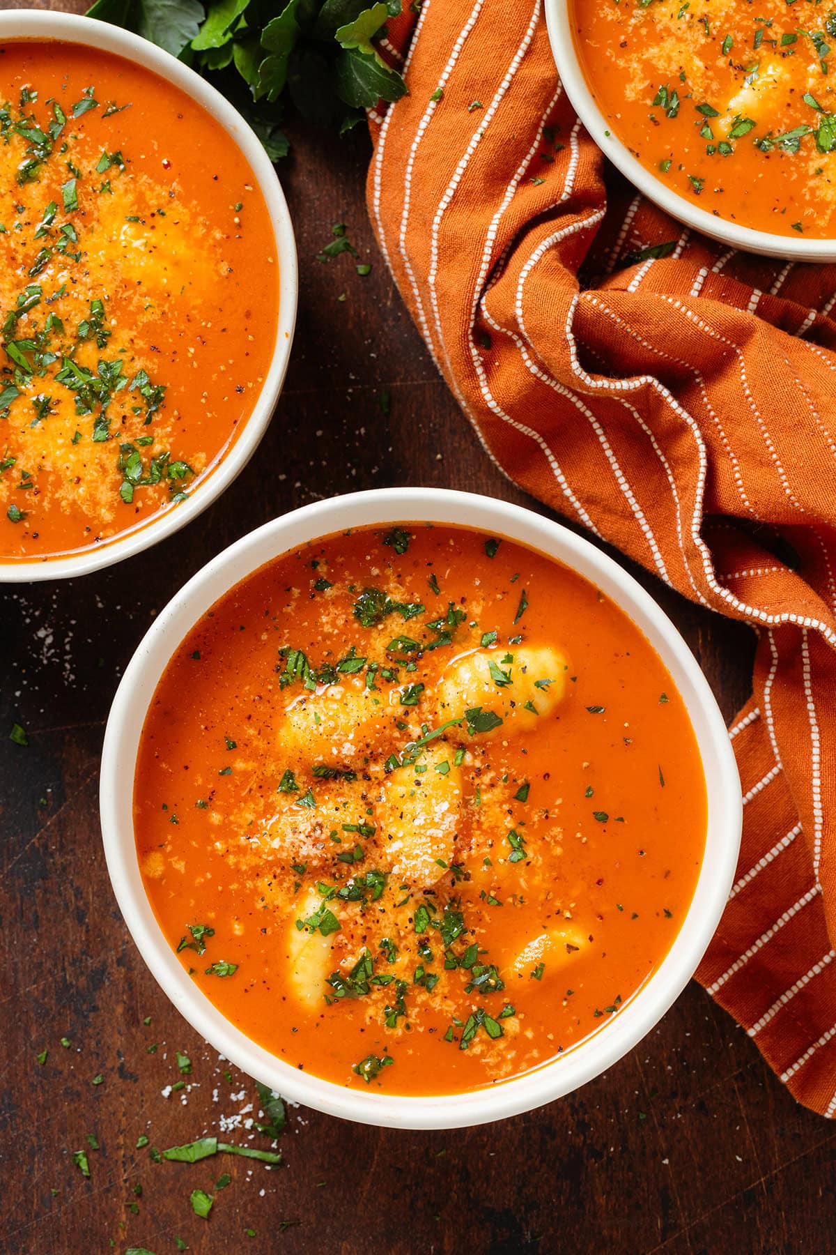 Creamy tomato gnocchi soup in white bowls garnished with fresh herbs and parmesan.