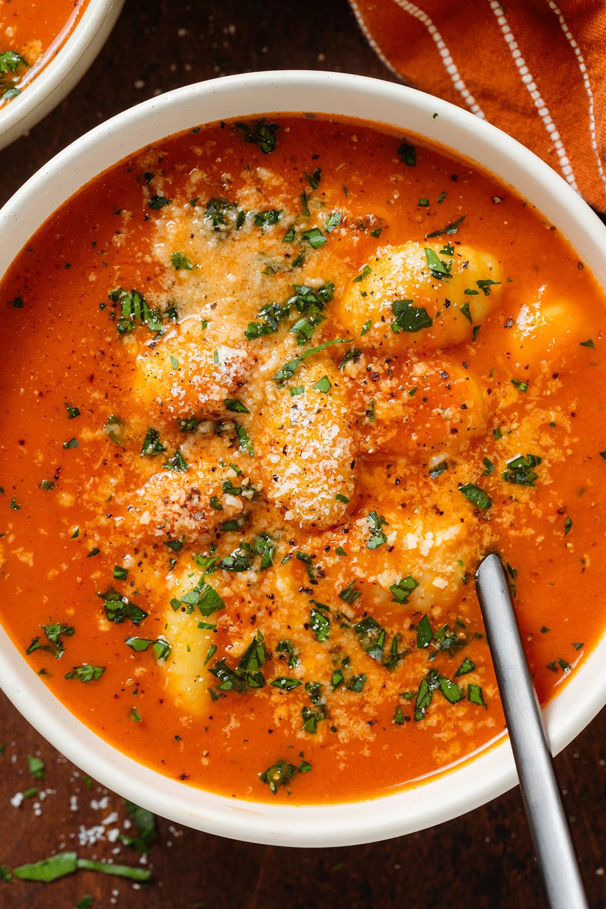 Creamy tomato gnocchi soup in a white bowl with a black spoon garnished with fresh herbs and parmesan.