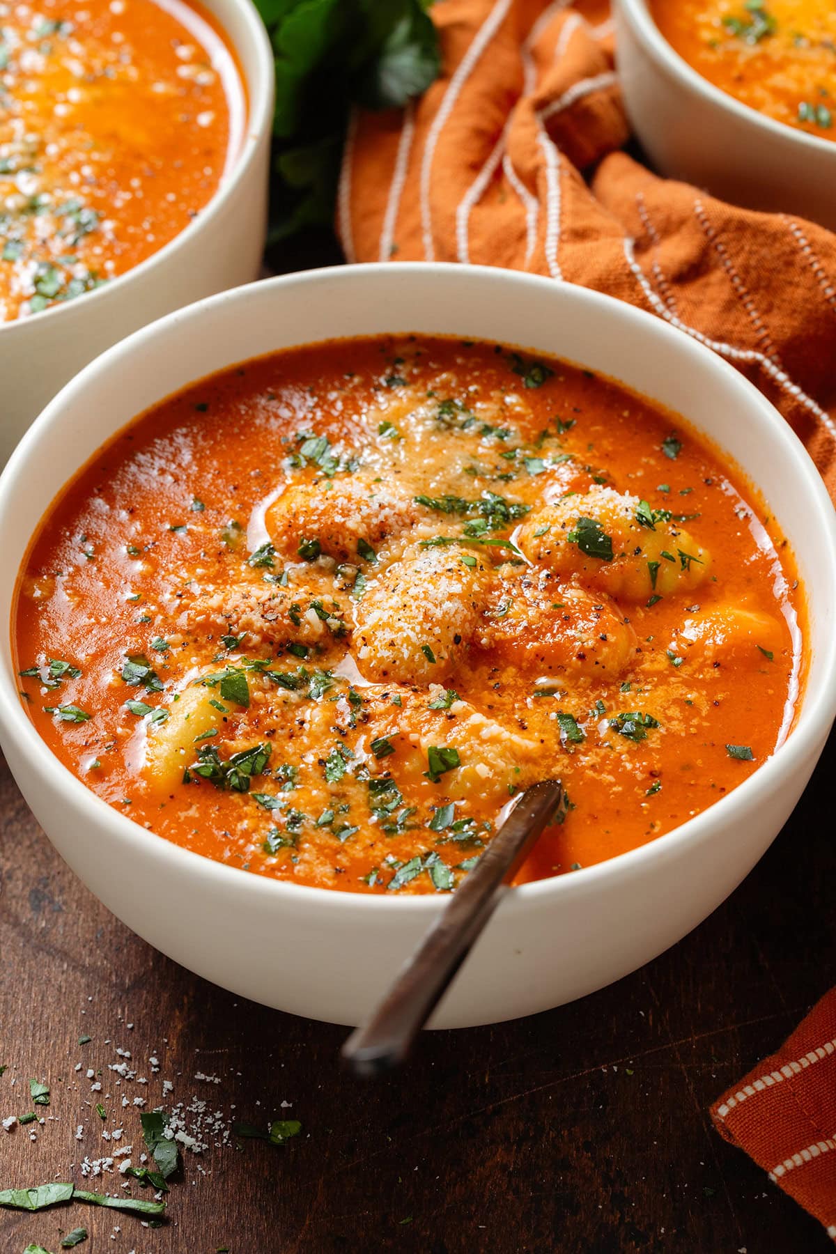 Creamy tomato gnocchi soup in a white bowl with a black spoon garnished with fresh herbs, black pepper, and parmesan.